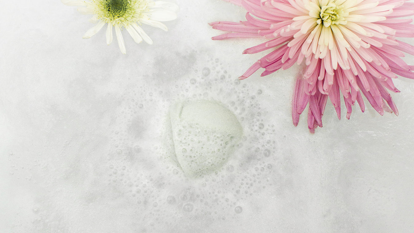 bath bomb dissolving in tub with pink and white flowers floating nearby
